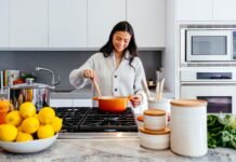 How to Choose the Right Kitchen Layout for Your Columbus Home A smiling woman preparing a meal in a modern kitchen in her Columbus home